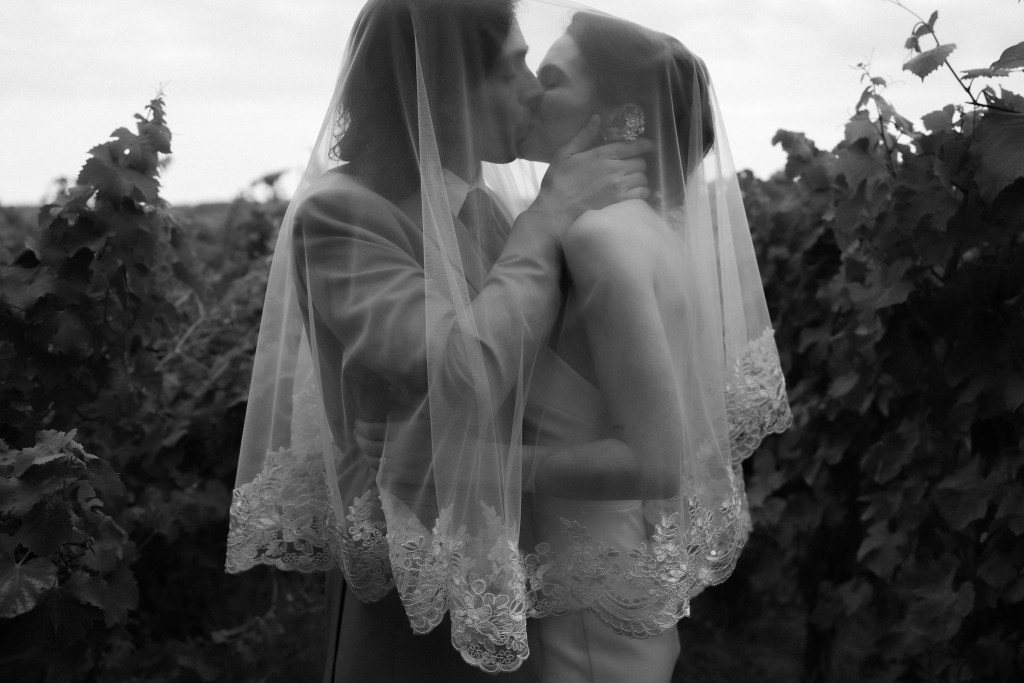 des mariés s'embrassent sour un voile au milieu de vignes